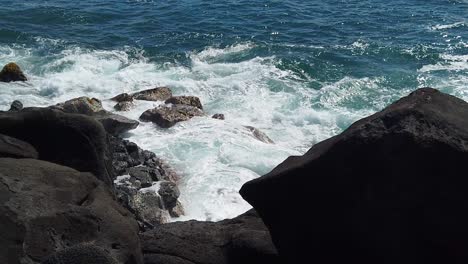 HD-Slow-motion-Hawaii-Kauai-looking-down-to-ocean-waves-swirling-and-building-and-crashing-on-rocks-below-with-lava-rocks-in-v-shaped-foreground-take-three