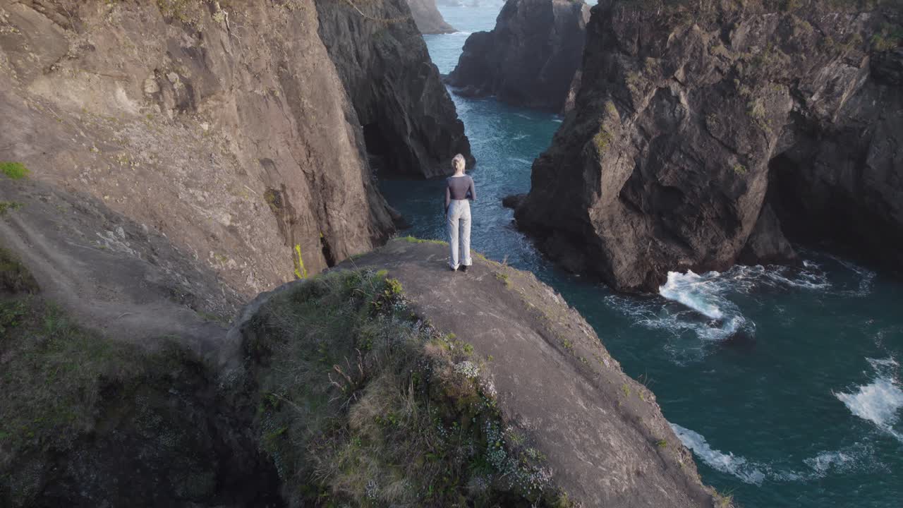 Woman standing on Natural Bridges Arch on Oregon's Ocean Coast - Aerial Tilt-up