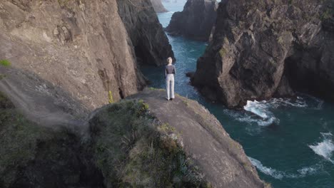 woman standing on natural bridges arch on oregon's ocean coast - aerial tilt-up