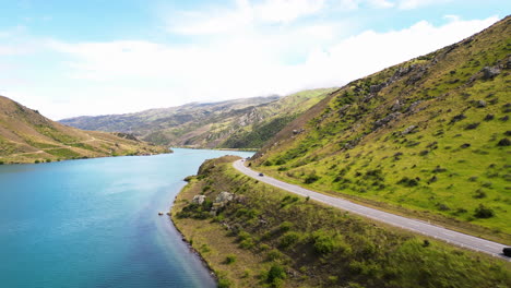 pequeños autos se mueven en una carretera que serpentea entre la montaña y la tranquila superficie de un fiordo, nueva zelanda