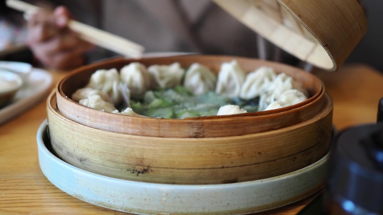 Person Opening Bamboo Steamer Basket Filled with Steaming Dumplings
