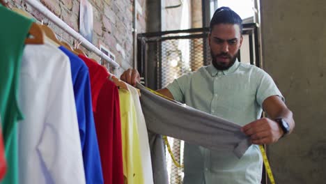 Mixed-race-male-fashion-designer-looking-at-different-clothes-and-smiling