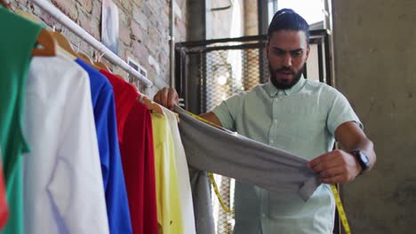 diseñador de moda masculino de raza mixta mirando diferentes ropas y sonriendo