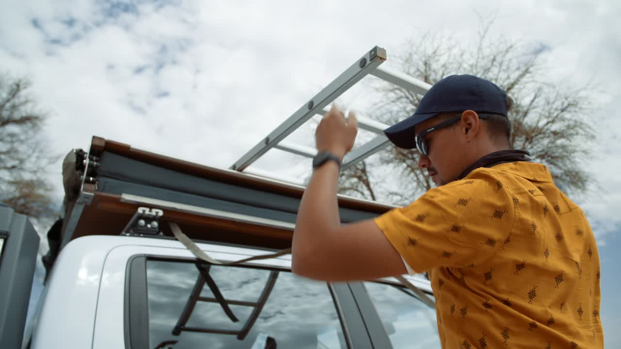 Handheld shot of a Caucasian male tourist in Africa closing a rooftop tent on top of a off-road vehicle on a windy campsite.