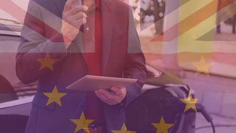 Flagge-Großbritanniens-Und-Der-Europäischen-Union-über-Einem-Mann,-Der-Ein-Tablet-Benutzt-Und-Ein-Elektroauto-Auflädt