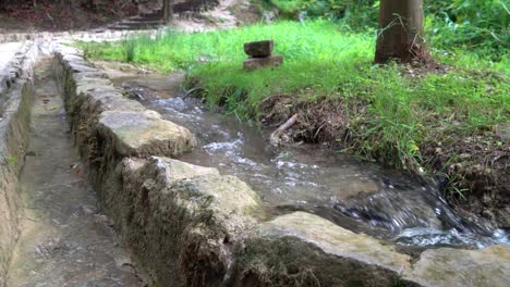 Water-flowing-next-to-a-stone-wall-along-a-walkway-at-Krka-National-Park-in-Croatia-at-¼-speed