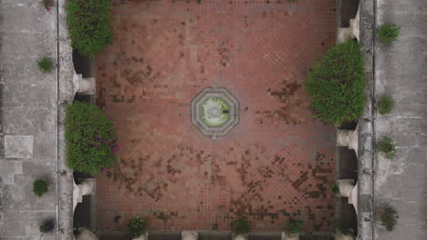 Aerial-top-down-footage-that-slowly-pulls-away-from-a-fountain-in-the-middle-of-a-historic-building-in-Antigua,-Guatemala