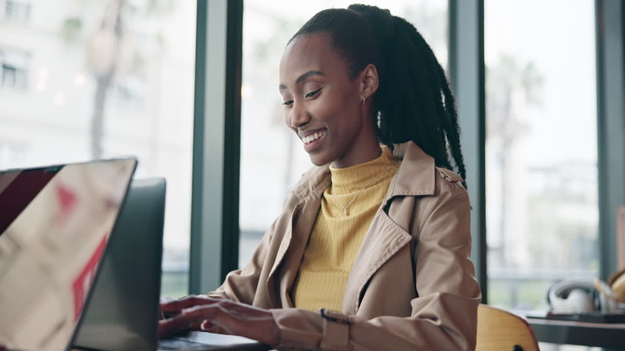 Happy black woman typing on laptop in cafe