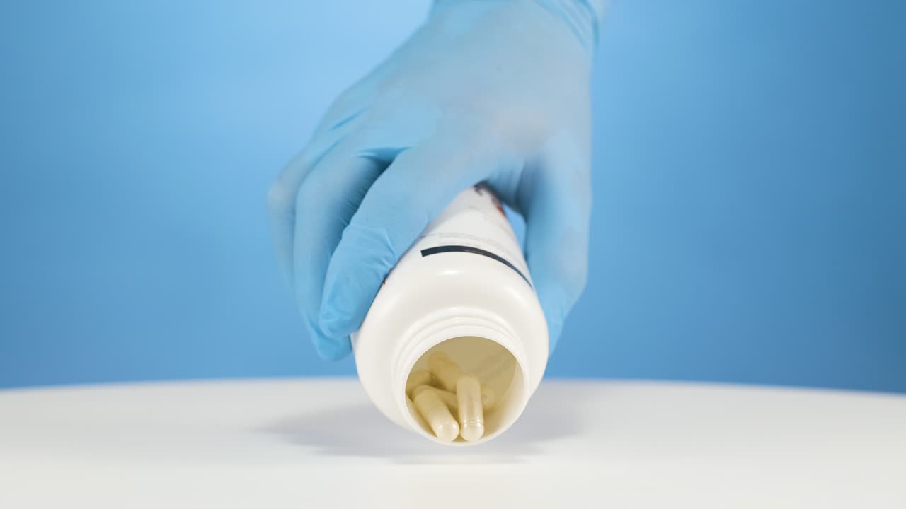 guantes azules vertiendo grandes cápsulas médicas blancas fuera del contenedor, cámara lenta