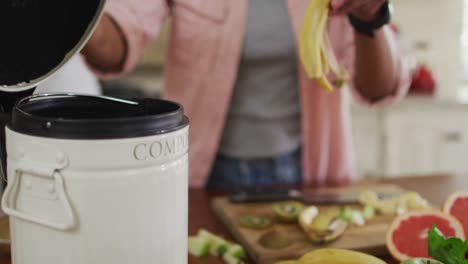 hands of biracial woman composting vegetable waste in kitchen