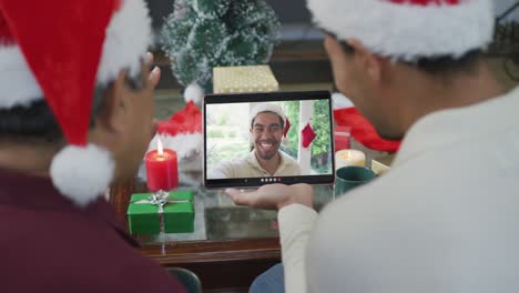 padre y hijo biraciales agitando y usando la tableta para la videollamada de navidad con el hombre en la pantalla