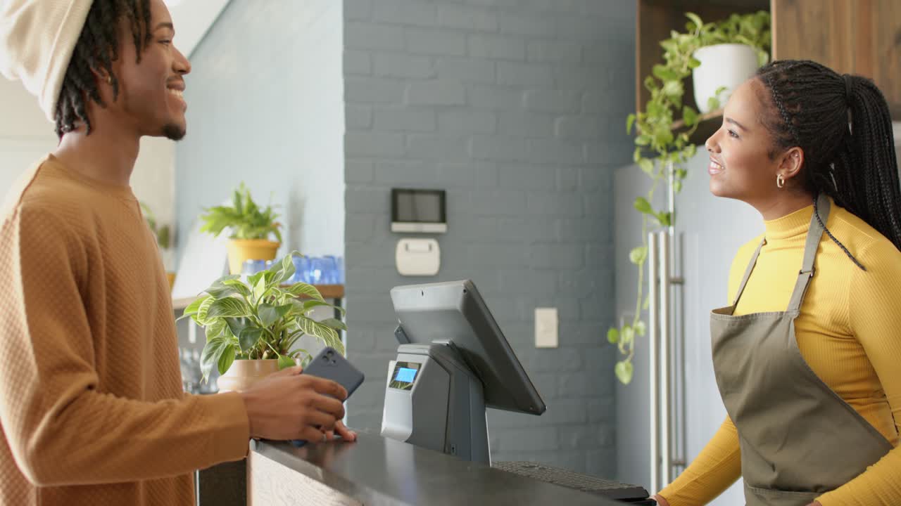 Afro-americano usando smartphone para pagamento enquanto o caixa escaneia no balcão do café