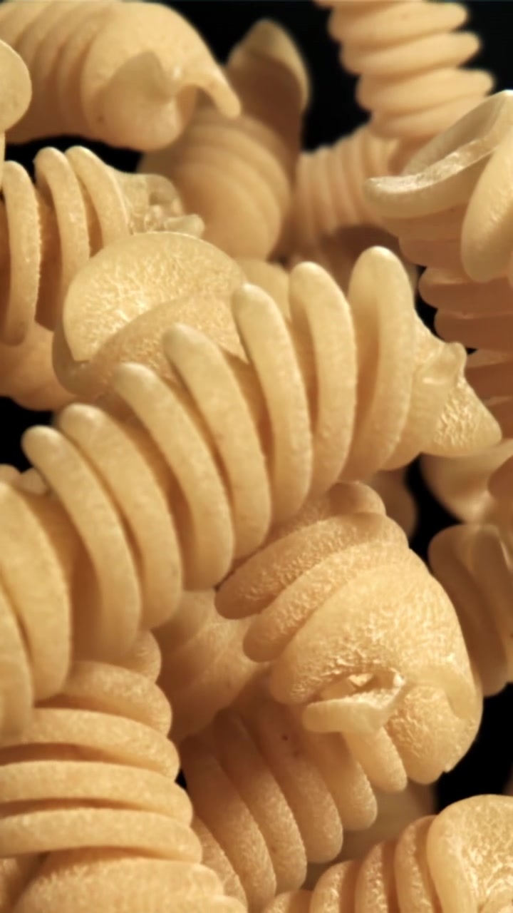 Macro Shot of Uncooked Fusilli Pasta Rising and Falling on Black Background