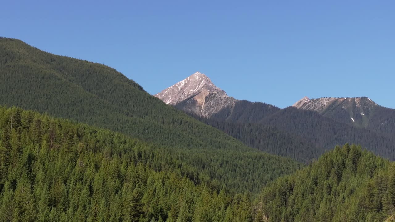Drone panning right revealing tall mountain and a vast pine forest wilderness near Banff and Yoho National Park in Canada under a partially cloudy sky