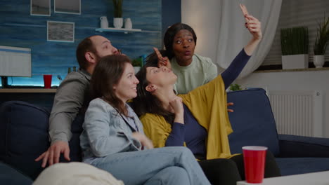 Excited-group-of-multiracial-friends-sitting-on-sofa-during-joyful-party