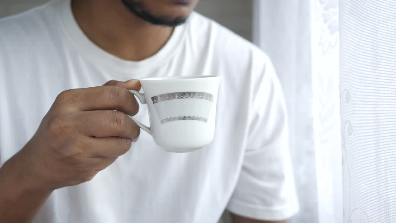 hombre sosteniendo una taza de café junto a la ventana
