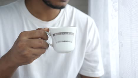 man holding coffee cup by the window