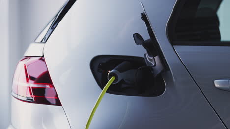 Primer-Plano-De-La-Mano-Conectando-El-Cable-De-Alimentación-A-Un-Coche-Eléctrico-Ecológico-De-Cero-Emisiones