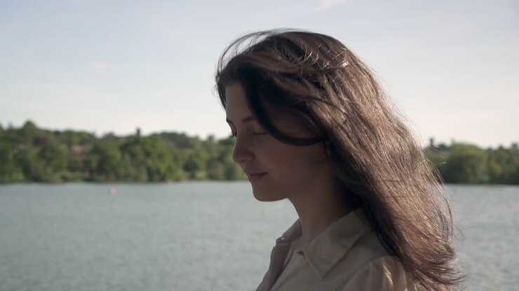 Ritratto al tramonto di un'adorabile e bellissima modella italiana che cammina accanto a un lago, indossando una camicia trasparente con colletto, guardandosi intorno, vagando e sentendosi libera