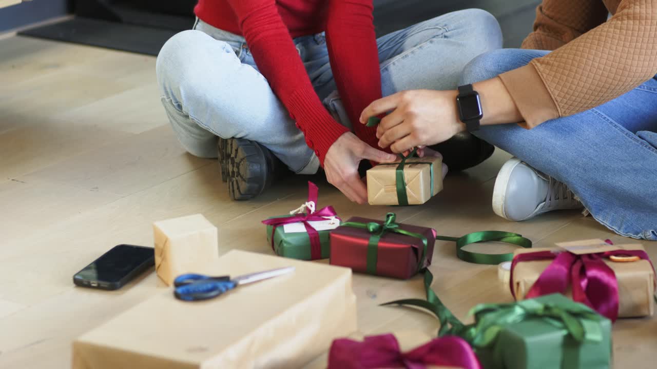 Mentre cerca una scatola in salotto, un gruppo di amici avvolge un nastro verde attorno ai regali.