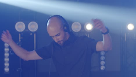 Live-DJ-performance-of-energetic-bald-man-with-headphones,-dancing-on-party-concert-musician-stage