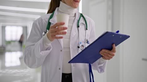doctor reviewing paperwork while drinking coffee in hospital hallway