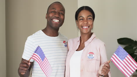 a diverse couple is beaming with pride, holding american flags and wearing vote stickers