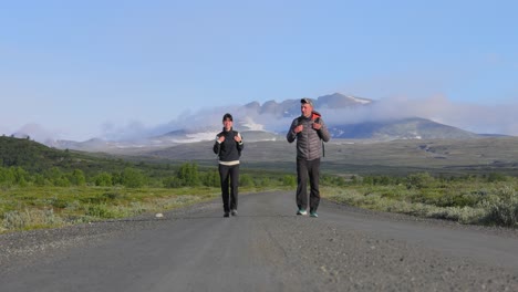 pareja de senderismo con mochilas en una carretera con montañas en el fondo. dovrefjell sunndalsfjella parque nacional es un parque nacional en noruega. hermosa naturaleza paisaje natural de noruega.