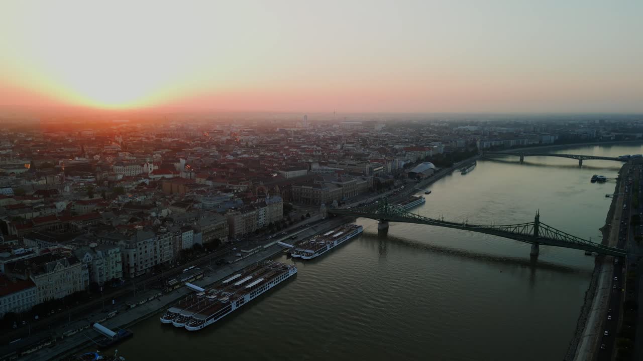 Morning drone above Budapest riverbanks and bridge with early sun casting shadows, panoramic establishing