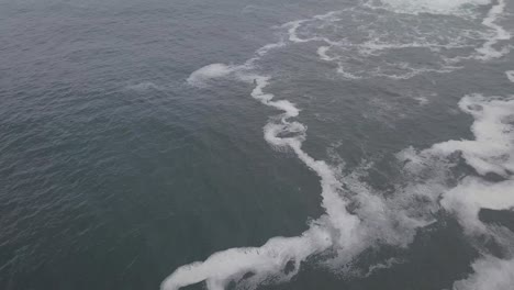 slow aerial tilt from seafoam to horizon on misty, grey indian ocean