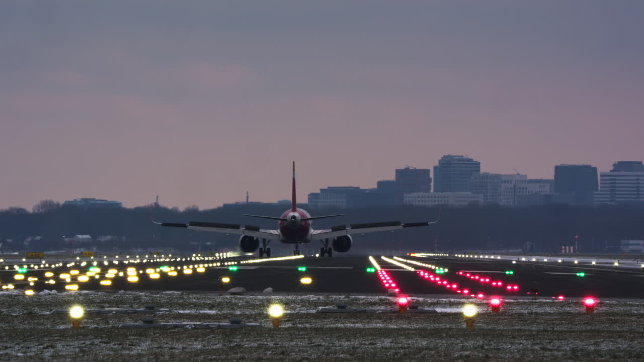 Avión comercial aterrizando en una pista de aeropuerto iluminada al anochecer.