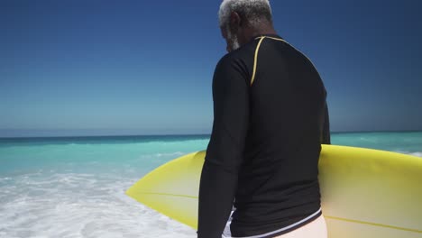 hombre mayor caminando con una tabla de surf en la playa