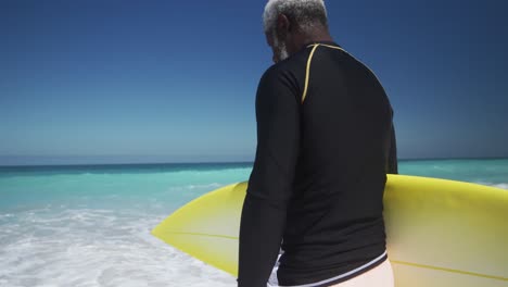 senior man walking with surfboard at the beach