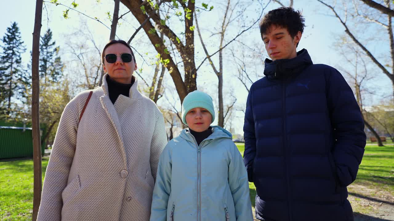 Famiglia di tre persone in piedi insieme in un parco soleggiato