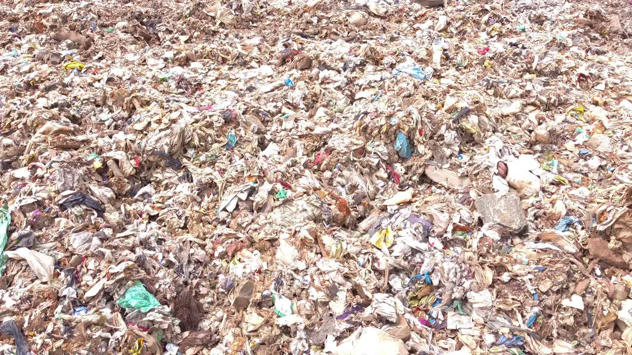 Close-up shot moving over an enormous pile of mixed waste, garbage, and trash spilling into a stagnant, polluted trench of water