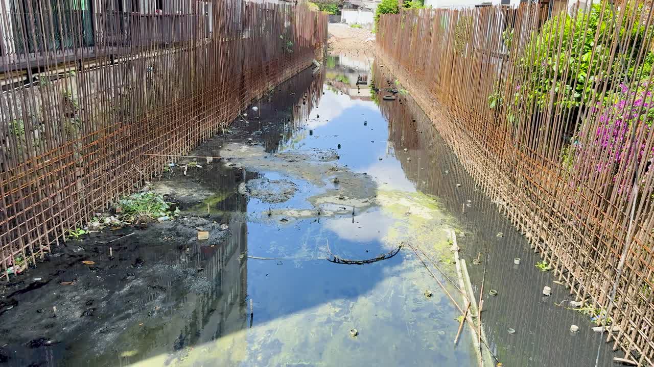 Daytime tracking shot of polluted canal, stagnant dirty water, and construction barriers in urban Phuket