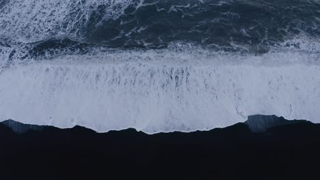 fierce waves of the atlantic hitting black sand beach in iceland - aerial straight down