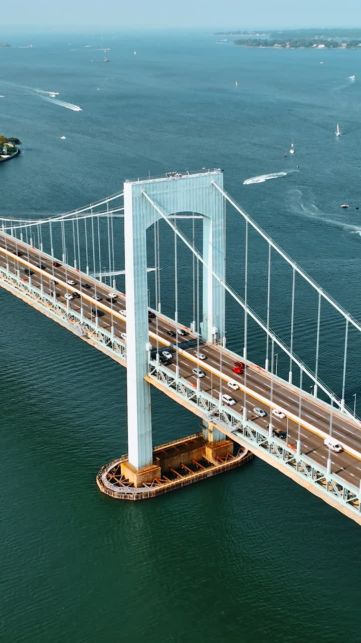 Lively traffic on the Throgs Neck Bridge on sunny day. View of the East River with multiple boats on. Aerial perspective. Vertical video
