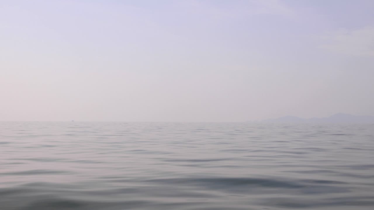 View from a ship travelling across a calm, foggy ocean.