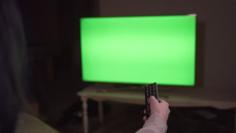 소녀는 그녀의 손에 리모컨, 크로마 키와 함께 저녁에 tv 앞에 앉아 있습니다