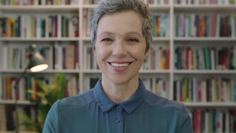 Retrato-De-Una-Mujer-Caucásica-Madura-Y-Amigable-Bibliotecaria-Sonriendo-Feliz-Disfrutando-De-Un-Hito-En-La-Educación-Profesional-Alegre-Mujer-De-Mediana-Edad-En-El-Fondo-De-La-Biblioteca