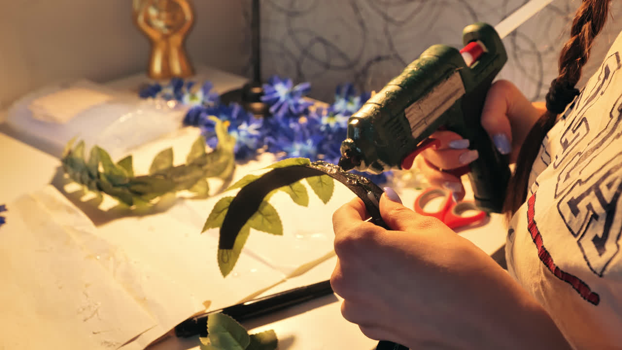 Close up of woman gluing artificial leaves to base of handmade flower crown