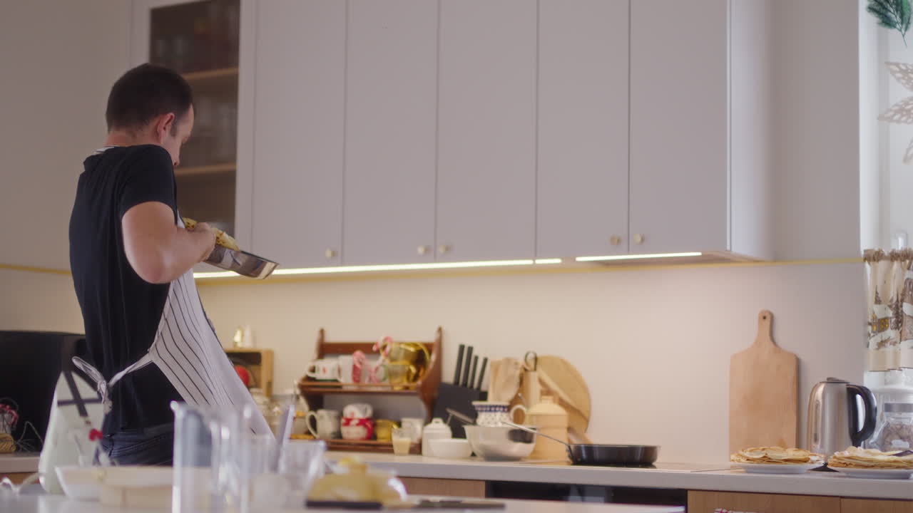 Un uomo fa cadere un pancake lanciandolo in alto mentre lavora in cucina.