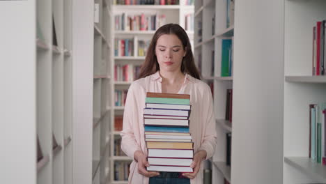 una mujer lleva una pila de libros en el almacén de la universidad. un joven bibliotecario reúne una pila de literatura para el cliente que camina entre las estanterías. educación de los estudiantes
