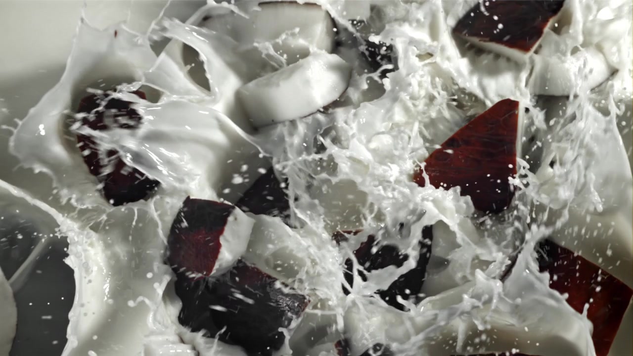 Pezzi di cocco fresco che schizzano in latte bianco cremoso al rallentatore