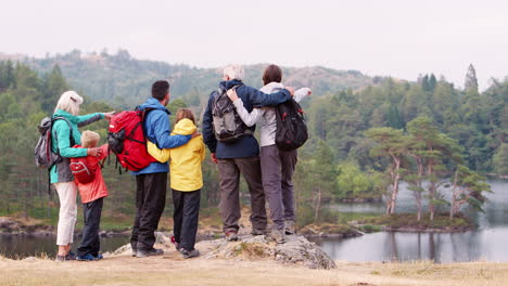 Multi-generation-family-embracing-and-admiring-the-lakeside-view,-back-view,-Lake-District,-UK