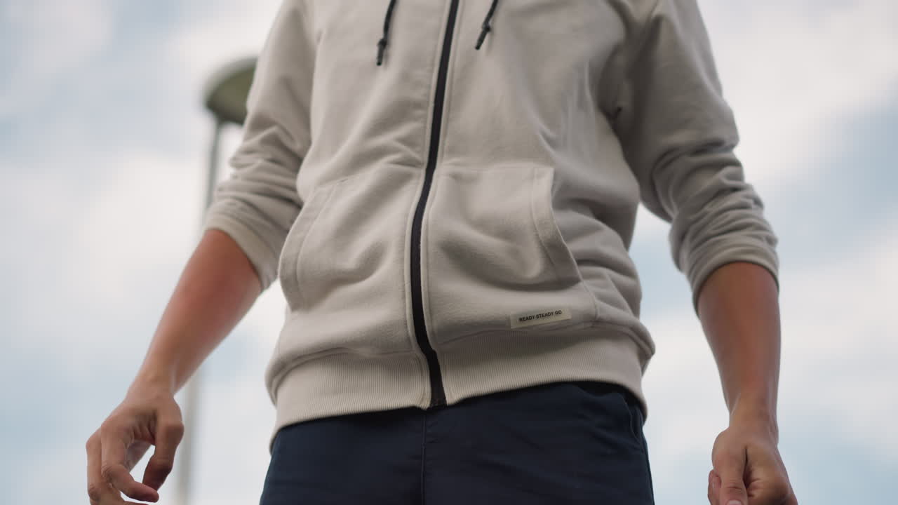 hombre remangándose bajo un cielo nublado, perspectiva baja mostrando los puños y las muñecas tensas, calentamiento urbano al aire libre con nubes espectaculares, la secuencia sugiere entrenador, atleta callejero y viajero preparándose