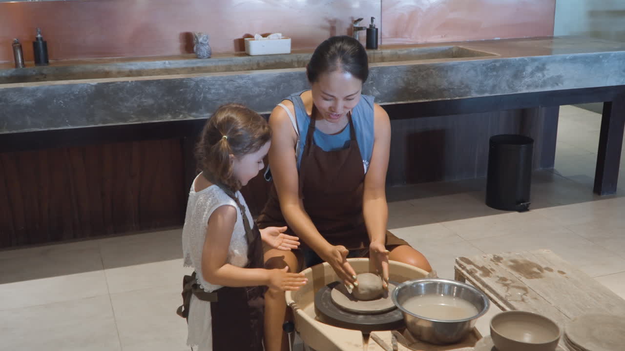 mujer y joven se reúnen alrededor de la rueda de alfareros formando arcilla juntos en el estudio riendo mientras añaden agua a la pelota