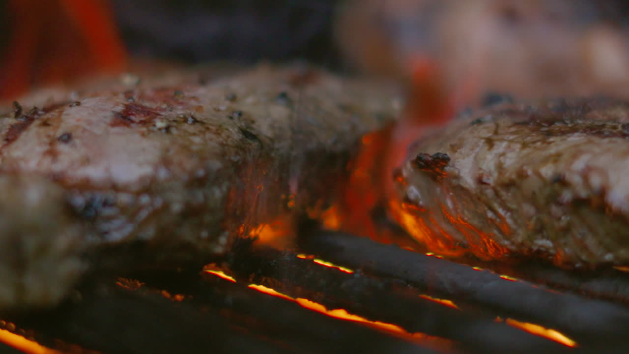 deliciosos filetes de filete siendo grillados a la llama en una barbacoa con fuego en el fondo y el chef moviendo la carne en la parrilla en cámara lenta 4k