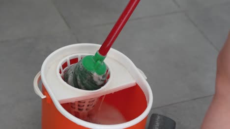 top-down close-up slow motion of a red bucket as the wet mop is wrung out in preparation for house cleaning